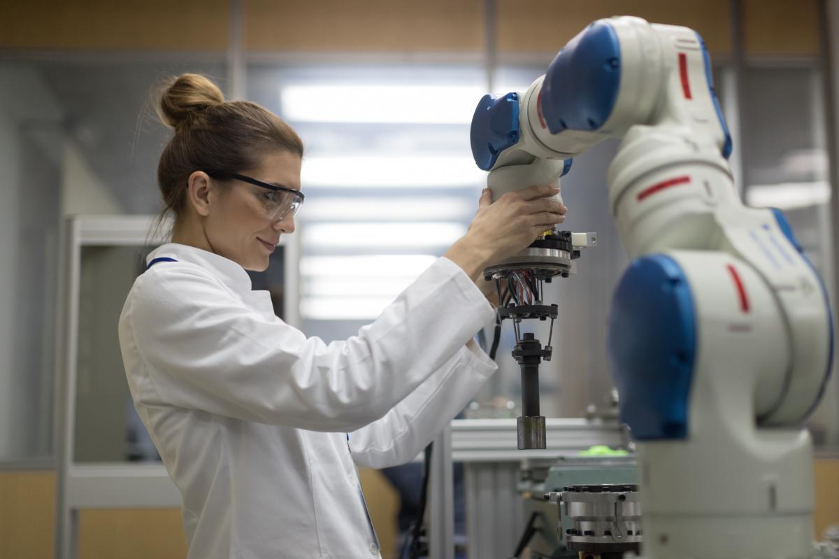 A female engineer in a white coat adjusts a collaborative robot.