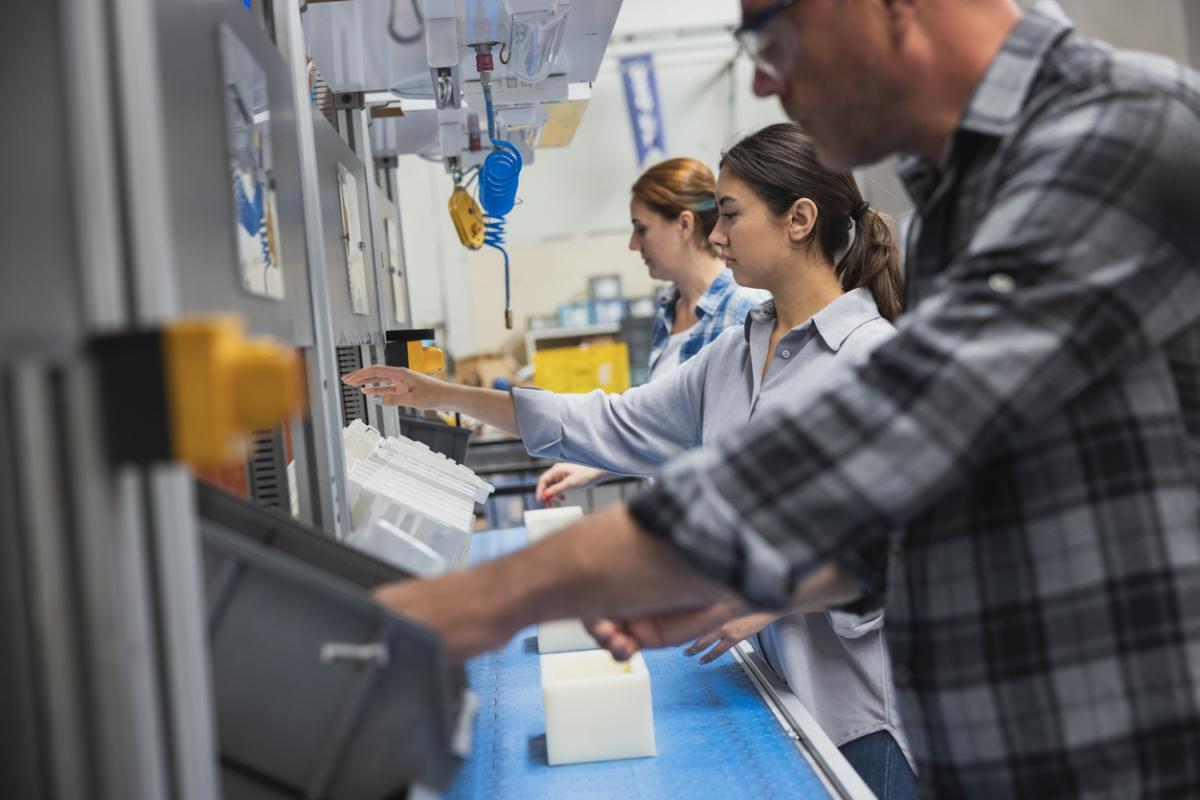 Industrial manufacturing employees lean over a workstation, performing skilled tasks.