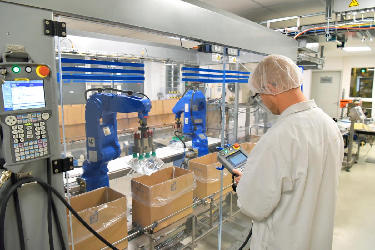 An employee in PPE inspects a screen at a workstation.